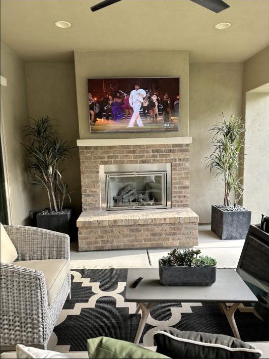 Outdoor patio TV mounted above a brick fireplace by Kalieb Designs