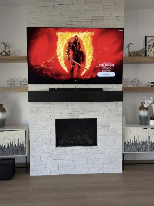 Soundbar mounted centered beneath a wall-mounted TV on a white stone accent wall, installed by Kalieb Designs